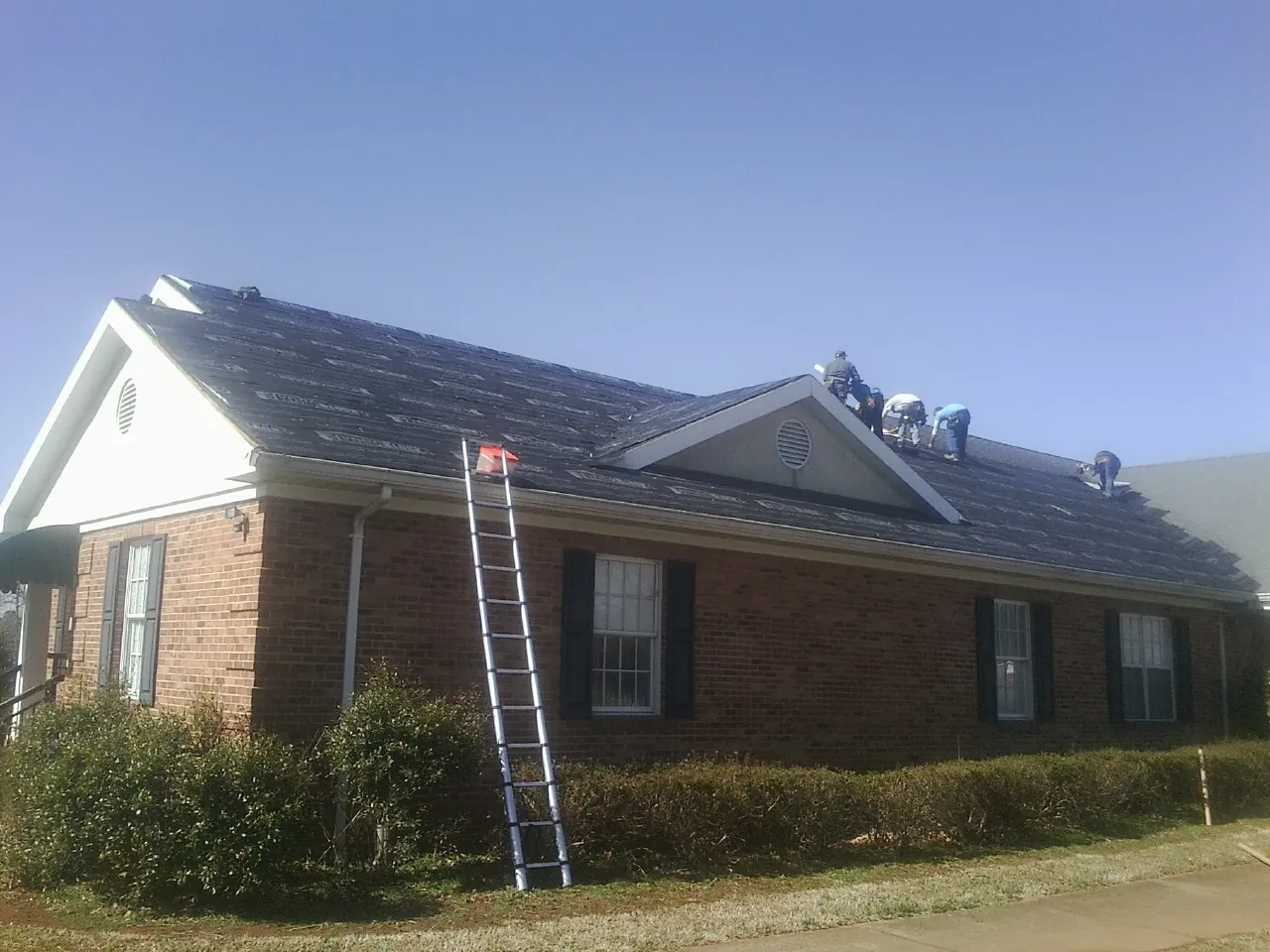 Crew tearing shingles off a brick ranch roof with a ladder set — Metal Roof Repair work by our crew in Zanesville