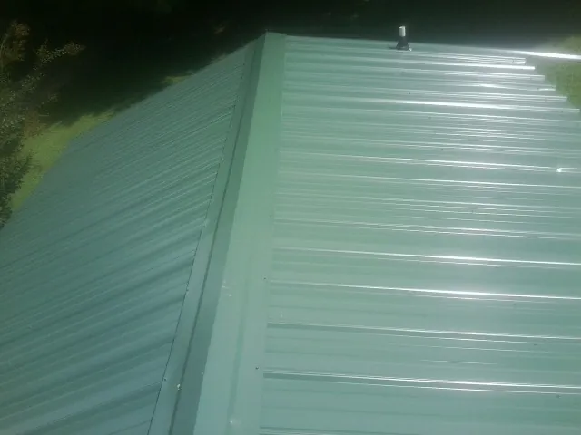 New green metal panels meeting at the ridge of a roof — Flat Roof Repair work by our crew in Zanesville