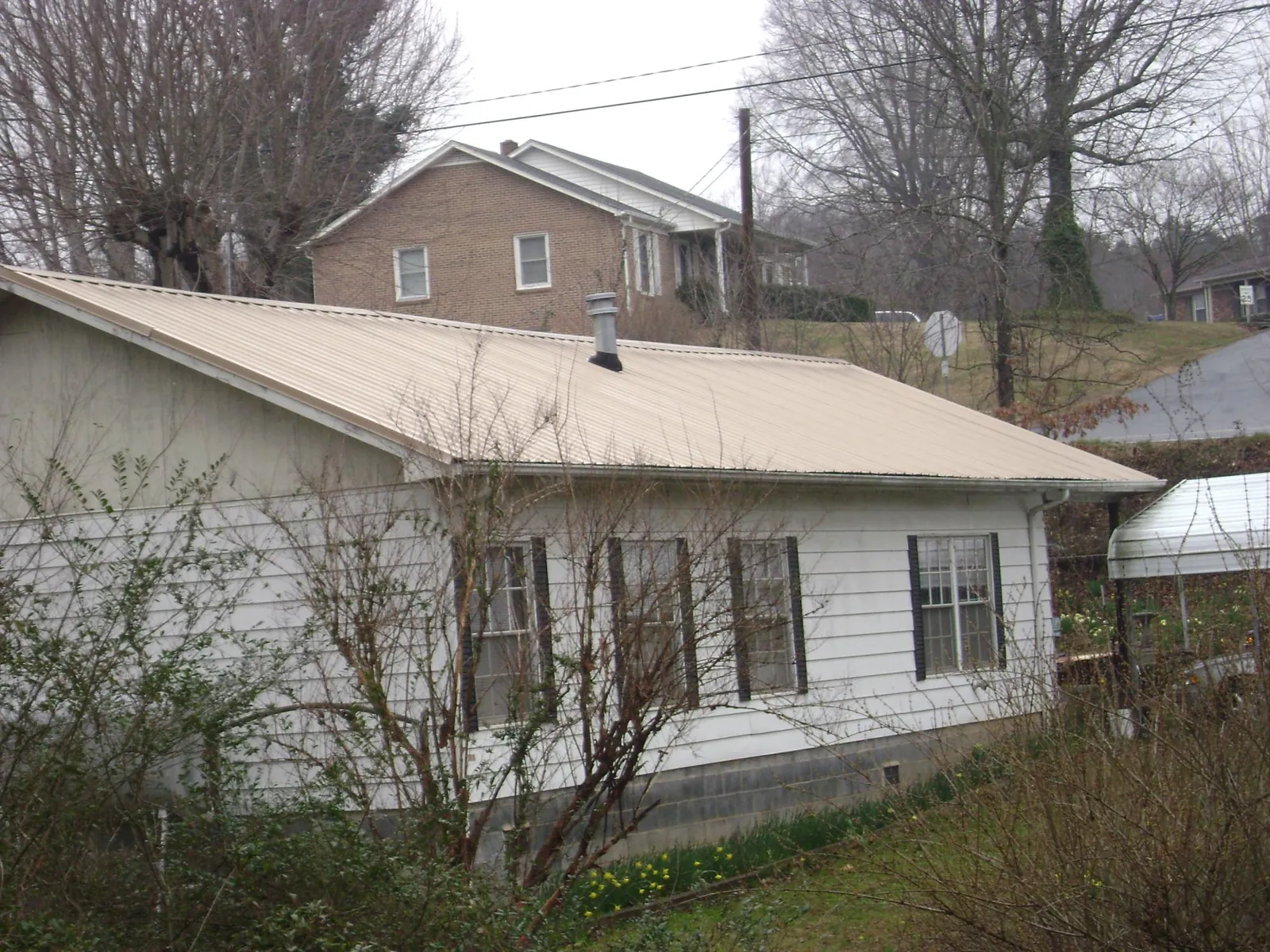 Tan metal roof on a white sided house set into a hillside — Commercial Roofing by Roofing Brothers in Zanesville